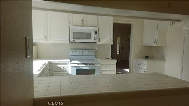 kitchen featuring tile counters, kitchen peninsula, white appliances, and white cabinetry