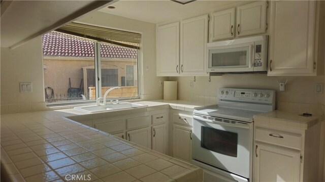 kitchen with tile counters, white cabinets, sink, and white appliances