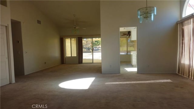 carpeted spare room with ceiling fan with notable chandelier, a towering ceiling, and plenty of natural light