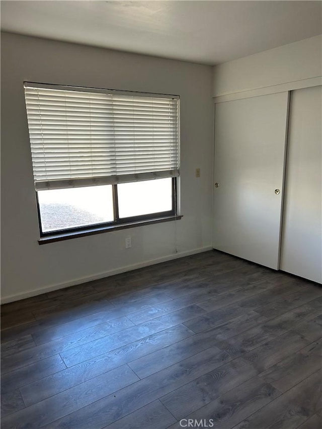 unfurnished bedroom featuring a closet, multiple windows, wood finished floors, and baseboards