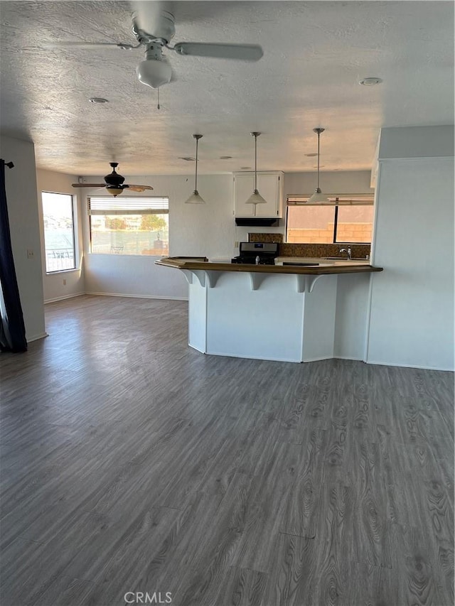 kitchen with dark wood finished floors, dark countertops, a breakfast bar, decorative light fixtures, and stainless steel gas range