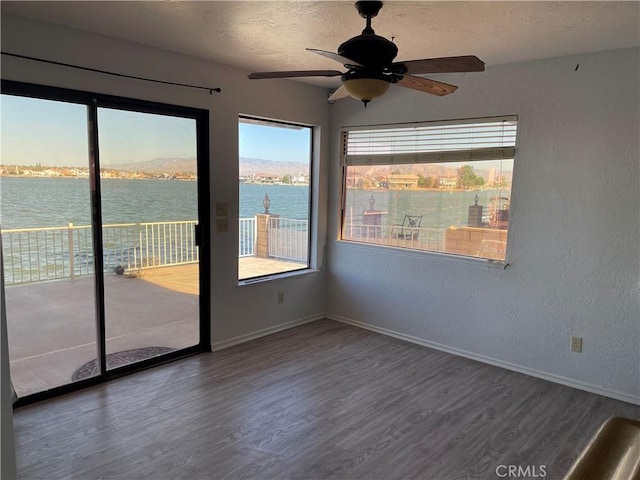 empty room with a water view, ceiling fan, dark hardwood / wood-style flooring, and a textured ceiling