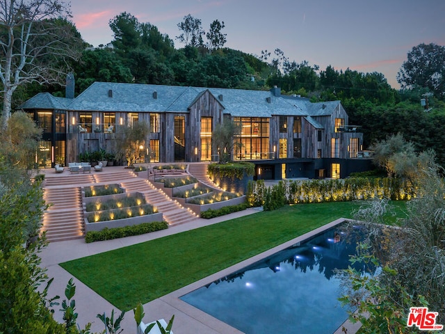 back house at dusk with a patio area and a yard