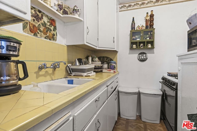 kitchen with tile countertops, white cabinetry, parquet flooring, black range with gas stovetop, and sink