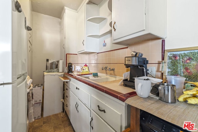 kitchen with white refrigerator, white cabinetry, tile counters, and sink