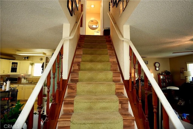 stairs featuring a wealth of natural light, a textured ceiling, and wood finished floors