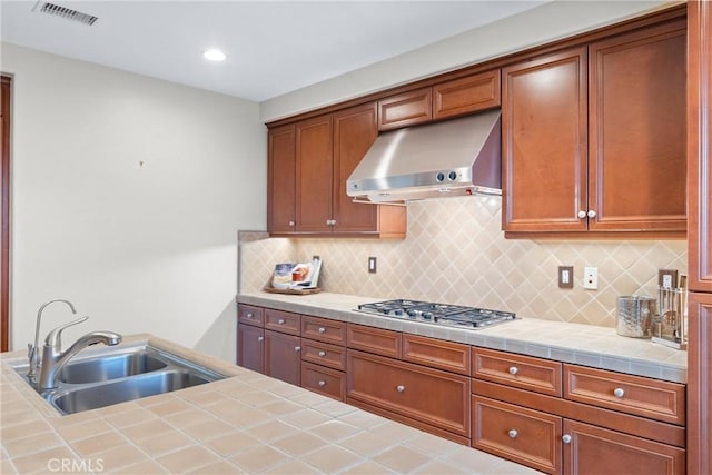 kitchen with stainless steel gas stovetop, tile countertops, tasteful backsplash, range hood, and sink