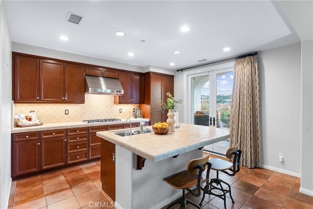 kitchen featuring sink, backsplash, stainless steel gas cooktop, a center island with sink, and a breakfast bar area