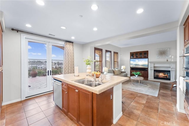 kitchen with stainless steel dishwasher, light tile patterned floors, a kitchen island with sink, and sink