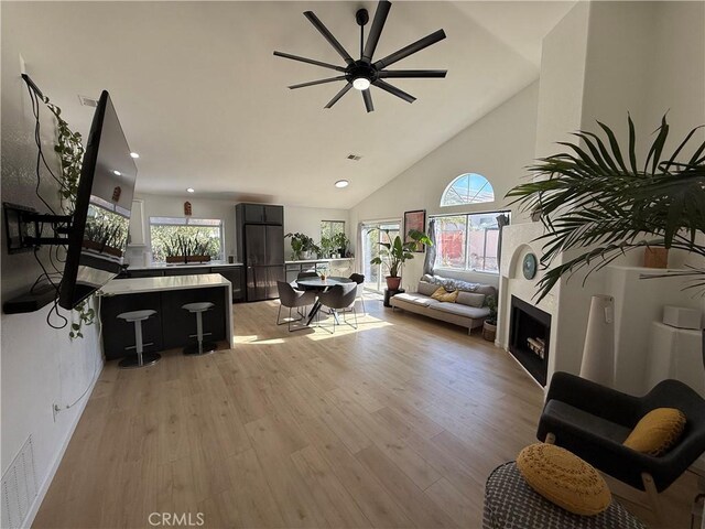 living room featuring ceiling fan, a healthy amount of sunlight, light wood-type flooring, and a high end fireplace