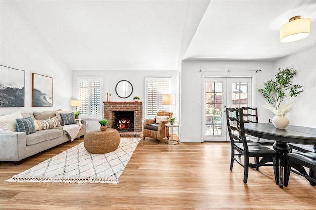 living room featuring light wood finished floors, baseboards, vaulted ceiling, french doors, and a brick fireplace