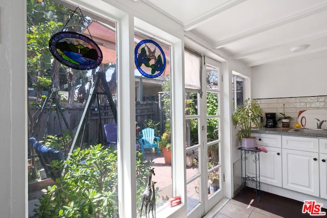 doorway with light tile patterned floors, plenty of natural light, and beamed ceiling