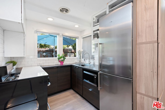 kitchen featuring dark brown cabinetry, appliances with stainless steel finishes, decorative backsplash, sink, and light wood-type flooring