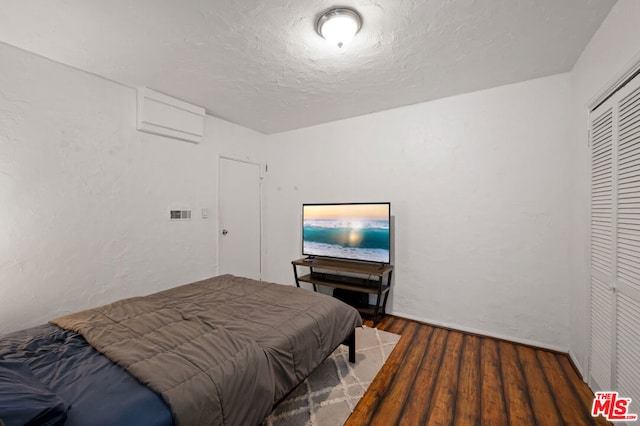 bedroom featuring a wall mounted AC, dark hardwood / wood-style flooring, a closet, and a textured ceiling