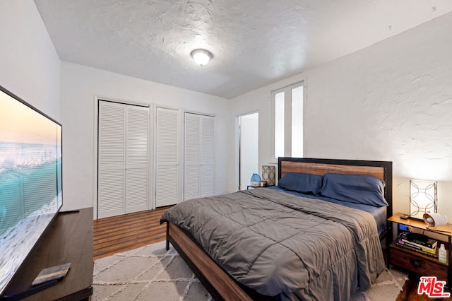 bedroom with two closets, a textured ceiling, and light wood-type flooring