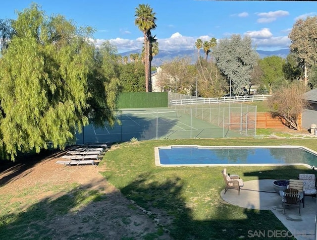 view of swimming pool with tennis court and a lawn