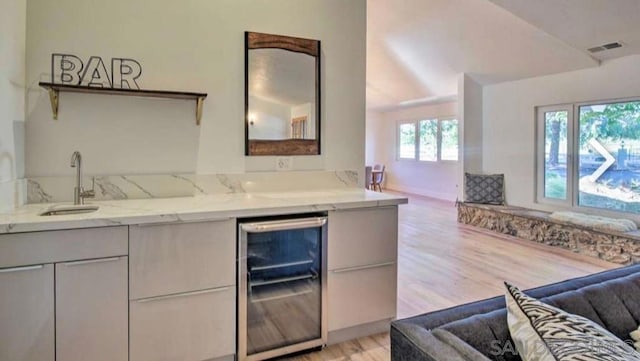 kitchen featuring light hardwood / wood-style flooring, beverage cooler, light stone counters, and sink