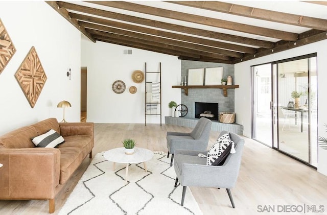 living room featuring a brick fireplace, light hardwood / wood-style floors, and vaulted ceiling with beams