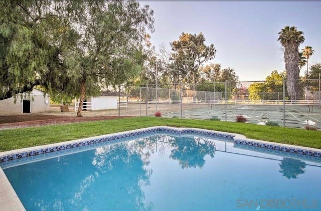 view of swimming pool with tennis court and a yard