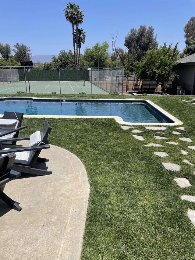 view of pool with tennis court and a lawn