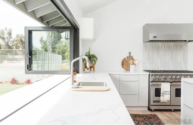 kitchen with exhaust hood, high end range, light stone countertops, white cabinets, and sink