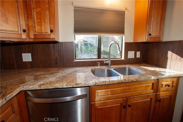 kitchen with stainless steel dishwasher, sink, and light stone counters