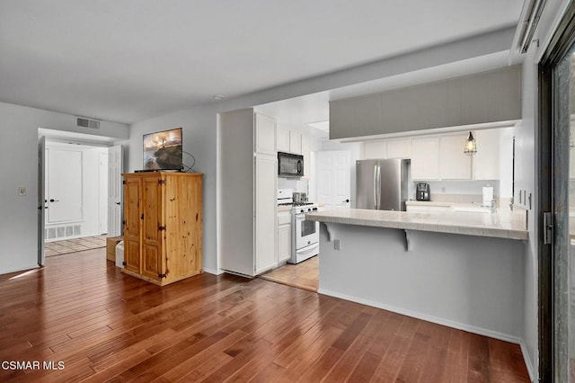 kitchen featuring kitchen peninsula, white range with gas stovetop, stainless steel fridge, and white cabinetry