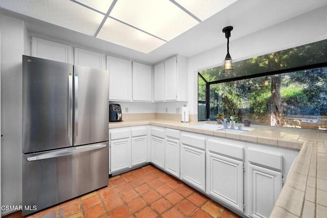 kitchen featuring white cabinetry, tile countertops, stainless steel fridge, and hanging light fixtures