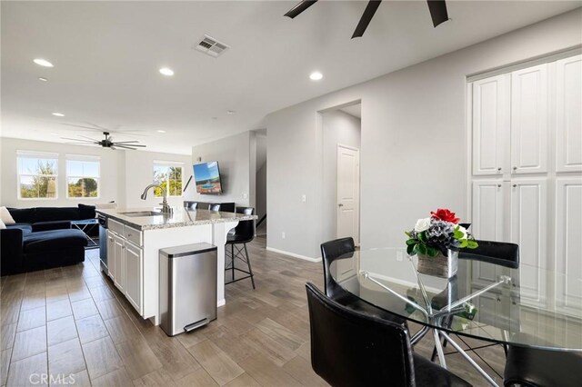 kitchen featuring ceiling fan, sink, white cabinetry, an island with sink, and light stone counters