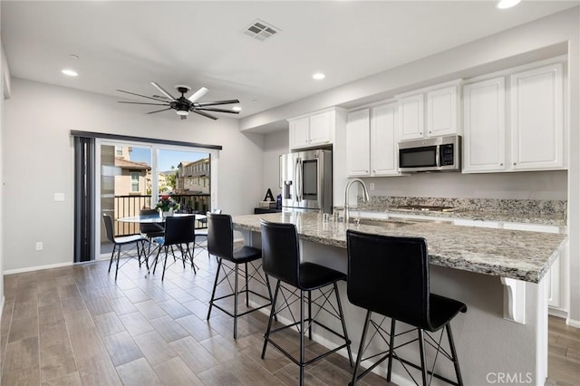 kitchen featuring a breakfast bar area, appliances with stainless steel finishes, ceiling fan, a spacious island, and white cabinets