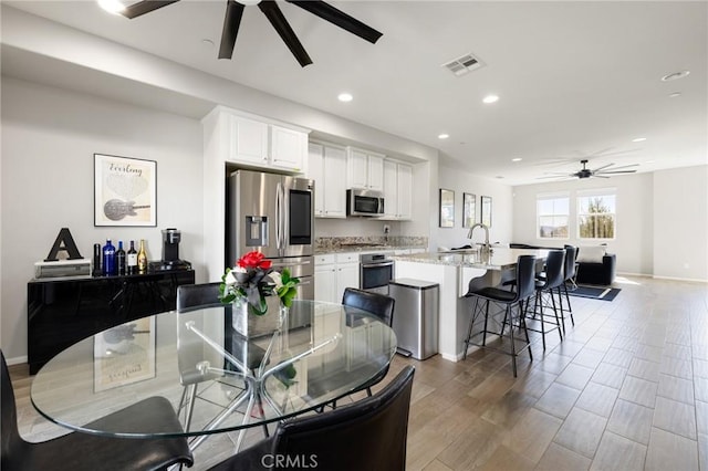 kitchen featuring white cabinetry, stainless steel appliances, a kitchen bar, and a center island with sink