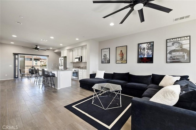 living room featuring ceiling fan, sink, and light hardwood / wood-style flooring