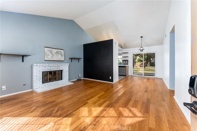 unfurnished living room featuring vaulted ceiling, a brick fireplace, and light hardwood / wood-style flooring