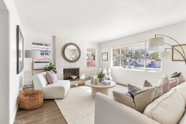 living room featuring a textured ceiling, a brick fireplace, cooling unit, and wood-type flooring