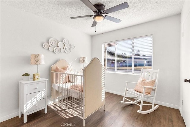 bedroom with ceiling fan, a nursery area, dark hardwood / wood-style flooring, and a textured ceiling