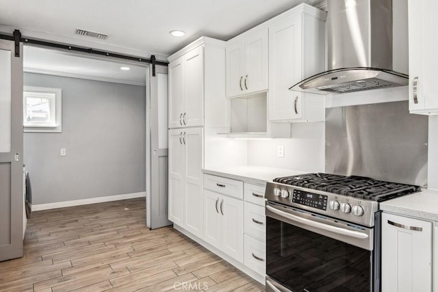 kitchen with white cabinets, a barn door, exhaust hood, and stainless steel range with gas cooktop