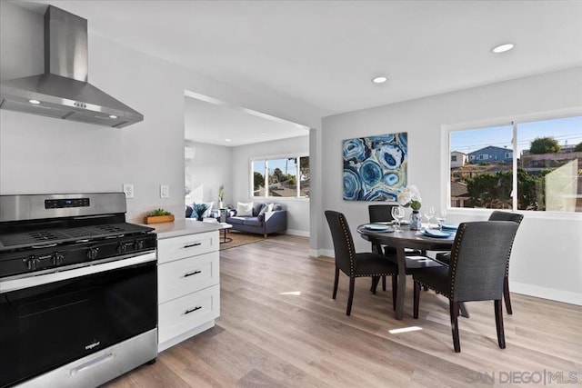 kitchen with wall chimney range hood, white cabinets, light wood-type flooring, and stainless steel gas range oven