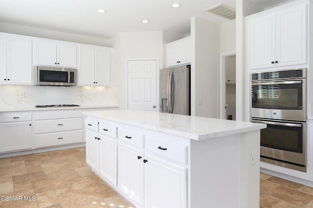 kitchen featuring white cabinetry, appliances with stainless steel finishes, decorative backsplash, light stone countertops, and a center island