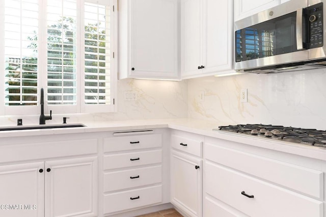 kitchen with appliances with stainless steel finishes, white cabinets, backsplash, and sink