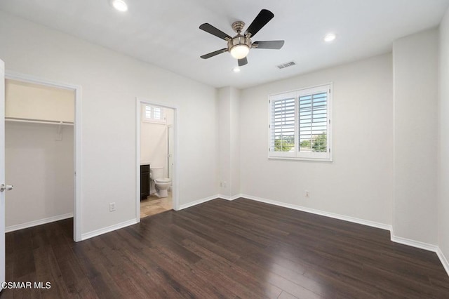 unfurnished bedroom featuring ceiling fan, connected bathroom, dark hardwood / wood-style floors, a closet, and a walk in closet