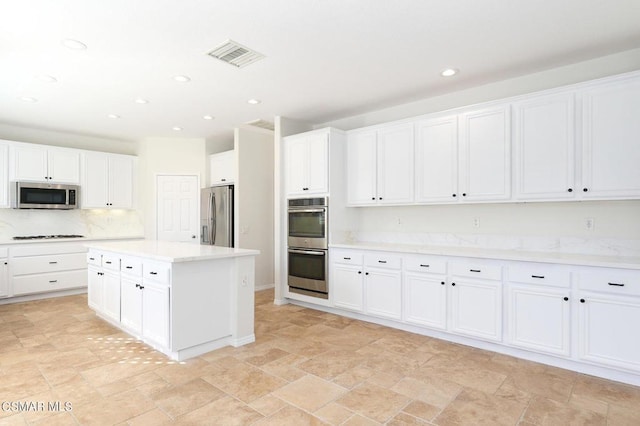 kitchen with a center island, light stone counters, stainless steel appliances, and white cabinetry