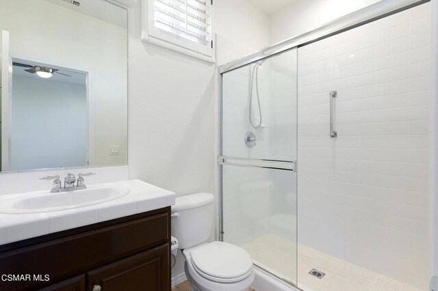 bathroom with toilet, vanity, ceiling fan, and a shower with shower door