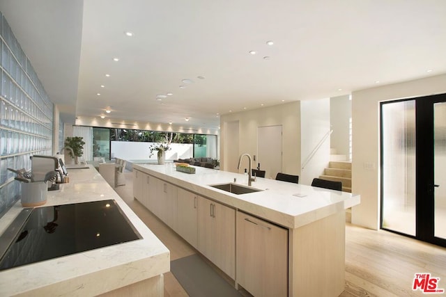 kitchen featuring sink, light wood-type flooring, light brown cabinets, a large island, and black electric cooktop