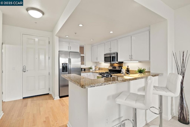 kitchen with kitchen peninsula, appliances with stainless steel finishes, white cabinets, and a breakfast bar area