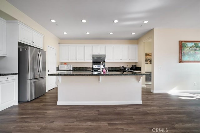 kitchen with white cabinetry, dark stone countertops, a center island with sink, and stainless steel refrigerator