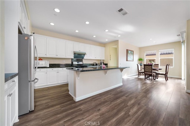 kitchen with white cabinetry, an island with sink, ventilation hood, appliances with stainless steel finishes, and a breakfast bar