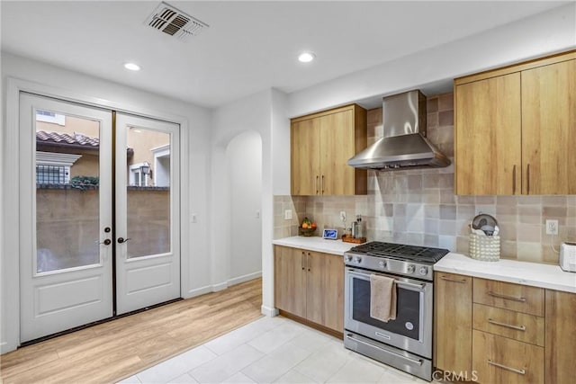 kitchen featuring backsplash, high end range, light wood-type flooring, french doors, and wall chimney exhaust hood