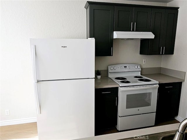 kitchen with dark cabinets, under cabinet range hood, white appliances, light countertops, and light wood-type flooring