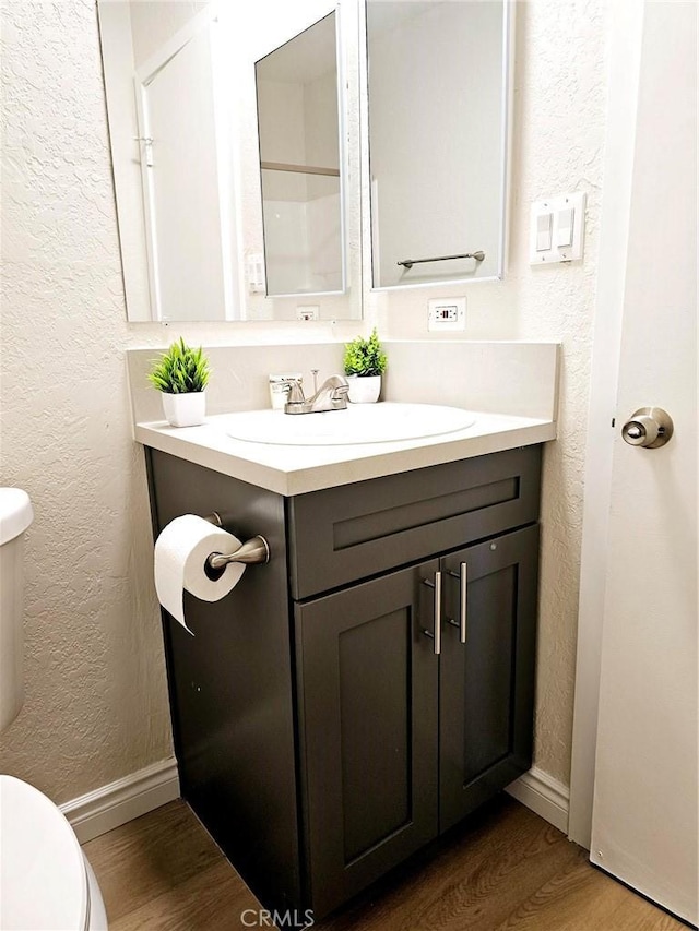 bathroom with toilet, vanity, wood finished floors, and a textured wall