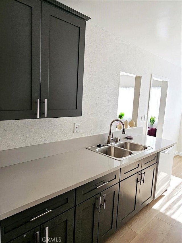 kitchen featuring a textured wall, light wood-style flooring, white dishwasher, light countertops, and a sink